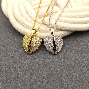 May include: Two angel wing necklaces, one gold and one silver, with clear crystal accents. The necklaces are on a white background.