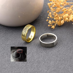 Peut inclure: Deux bagues, une dorée et une argentée, avec des surfaces texturées. La bague dorée porte l'inscription "Mott". La bague argentée porte l'inscription "Bonnie". Une petite image d'un nez de chien est dans le coin inférieur gauche.