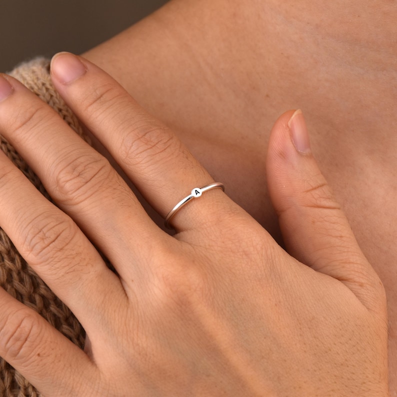 May include: A silver ring with a small letter "A" on it. The ring is worn on a person's finger.