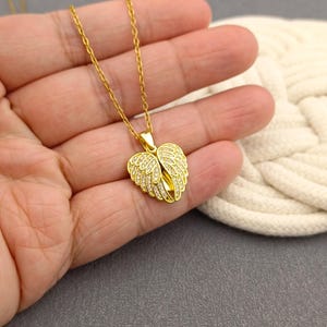 May include: A gold chain necklace with a heart-shaped pendant featuring angel wings adorned with sparkling clear stones.