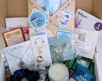 May include: A gift box containing a selection of items such as a necklace, a keychain, a candle, tea, chocolate, and stickers. The box features blue and gold accents, with a sticker reading "For Booklovers".
