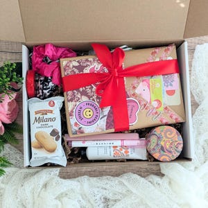 May include: A gift box filled with various items, including a wrapped package tied with a red ribbon, a package of Milano dark chocolate cookies, and a pink scrunchie. The box contains stickers that say "Probably Reading" and "Enemies to Lovers".