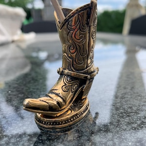May include: A gold cowboy boot shaped toothpick holder with two toothpicks sticking out of the top.