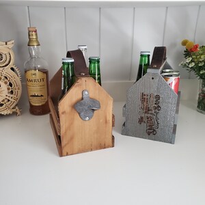 May include: Two wooden six-pack beer carriers. One is natural wood with a bottle opener and the other is gray with the text "Ours & Sand" printed on it.
