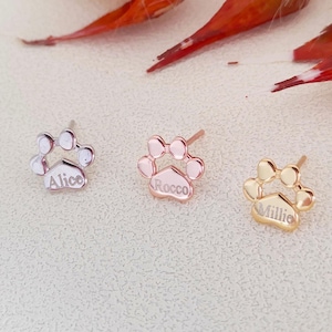 Op de afbeelding: Drie zilveren, roségouden en gouden oorbellen in de vorm van een poot met de gegraveerde namen "Alice", "Rocco" en "Millie".