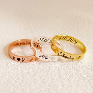 May include: Three personalized rings with heart cutouts. The gold ring says "Theodore" and "4.10.2019". The silver ring says "Alfie" and "07.18.20". The rose gold ring says "love you forever" and "K M".