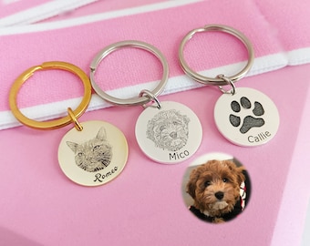 Puede incluir: Tres llaveros de plata con imágenes grabadas. El llavero de la izquierda tiene la cara de un gato y el nombre "Romeo" grabado en él. El llavero del medio tiene la cara de un perro y el nombre "Mico" grabado en él. El llavero de la derecha tiene una huella de pata y el nombre "Callie" grabado en él.