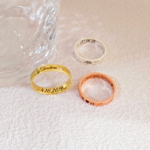 May include: Three personalized rings with engraved text. The gold ring says "Theodore" and "4.10.2019". The rose gold ring says "love you forever" and "K & M". The silver ring says "Alfie" and "07.18.21".