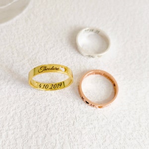 May include: Three gold, silver, and rose gold rings with personalized engravings. The gold ring says "Theodore" with a heart cutout and the date "4.10.2019". The rose gold ring says "love you forever" and has a heart cutout. The silver ring has a heart cutout and the date "11.18.21".