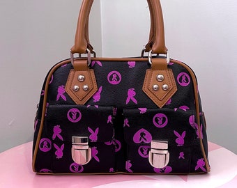 Peut inclure: Un sac à main noir de style cartable avec des finitions en cuir marron et des logos de lapin rose. Le sac a deux poches avant avec des fermoirs argentés.