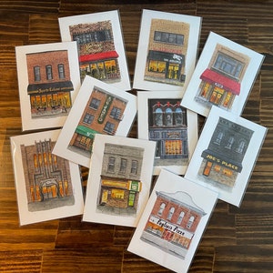 May include: A set of ten watercolor illustrations of storefront buildings. Each illustration features a different building with a unique name and design. The illustrations are painted in a realistic style with a focus on detail. The buildings are all in a similar style, with brick walls, wooden doors, and windows. The illustrations are perfect for adding a touch of whimsy to any home or office.