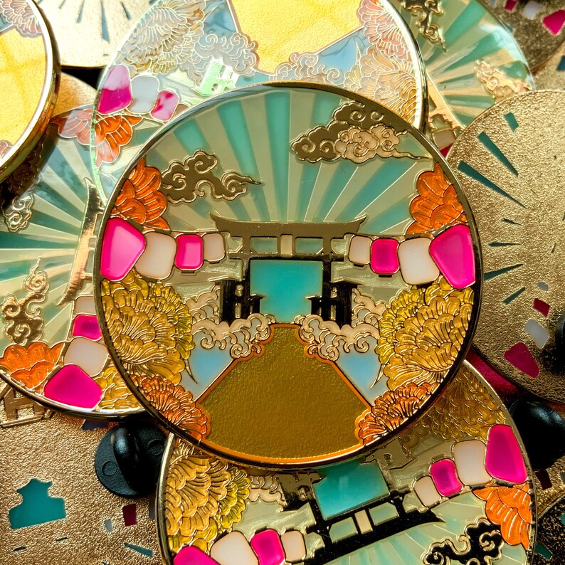 以下が含まれることがあります： 日本の伝統的な鳥居、雲、花を細部まで描いた金色のエナメルピン。鳥居は日本の神社によく見られる伝統的なものです。ピンは青と緑の色合いで、金色のアクセントが施されています。