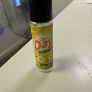 May include: A roll-on perfume bottle with a black cap and a yellow and green label. The label features the words "Clean Day" in red and white, along with floral graphics. The bottle contains 10 ml / 0.33 fl oz of perfume.