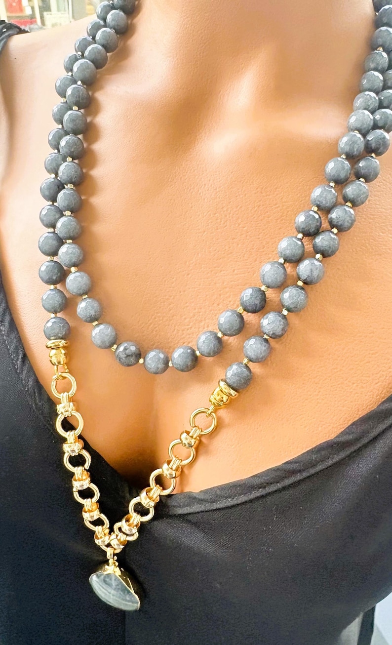 Puede incluir: Un collar de doble hebra con cuentas grises facetadas y detalles en metal dorado. El collar incluye una secci&oacute;n de cadena de eslabones gruesos en tono dorado que se conecta a un colgante de piedra gris, creando una apariencia de capas.