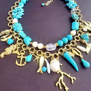 May include: A gold-toned necklace featuring turquoise beads, coral, and charms. The necklace includes a seahorse, anchor, fish, and coral branch pendants. Additional elements include white pearls and clear crystal beads.