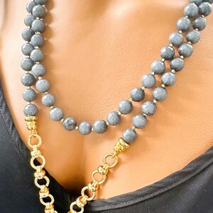 Puede incluir: Un collar de doble hebra con cuentas grises facetadas y detalles en metal dorado. El collar incluye una secci&oacute;n de cadena de eslabones gruesos en tono dorado que se conecta a un colgante de piedra gris, creando una apariencia de capas.