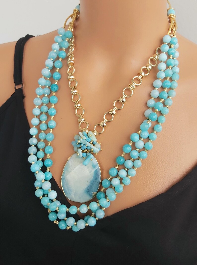 May include: A multi-strand necklace with a large blue and white agate pendant. The necklace is made of light blue and turquoise beads and a gold chain.