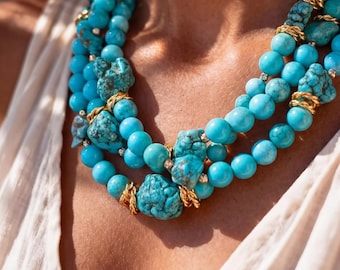 May include: A multi-strand necklace featuring bright turquoise beads and irregular, raw turquoise stones. The strands are accented with small, textured gold-tone metal spacers and links, creating a layered look with vibrant blue and gold tones.