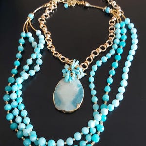 May include: A layered necklace with turquoise beads and a large turquoise pendant. The necklace is made of gold chain and turquoise beads.
