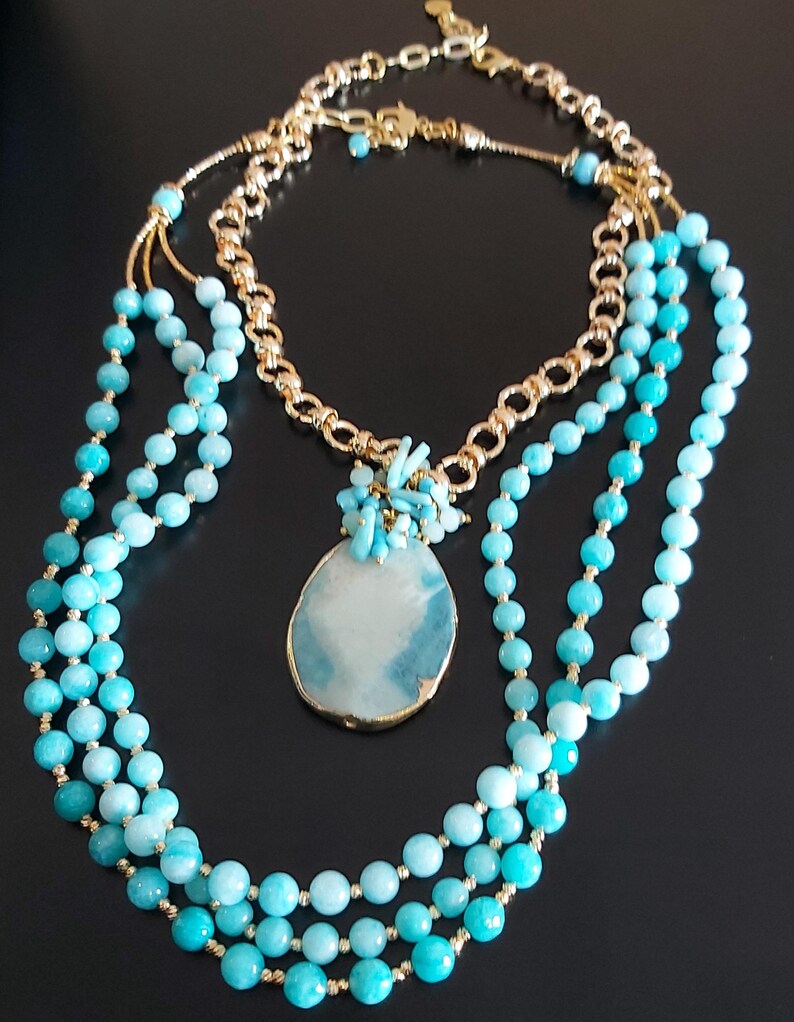 May include: A layered necklace with turquoise beads and a large turquoise pendant. The necklace is made of gold chain and turquoise beads.