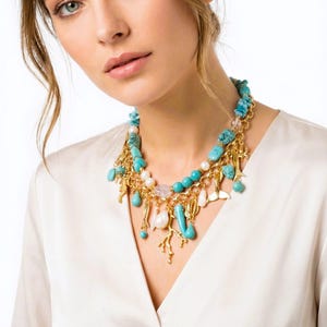 May include: A turquoise and gold necklace with various charms, including pearls, coral, and small gold pendants. The necklace is layered and features a mix of textures and shapes, creating a statement piece.