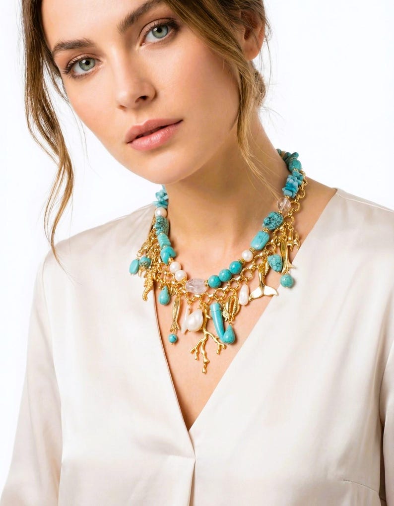 May include: A turquoise and gold necklace with various charms, including pearls, coral, and small gold pendants. The necklace is layered and features a mix of textures and shapes, creating a statement piece.