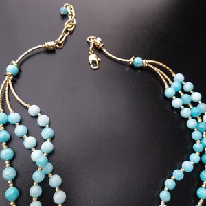 May include: A three-strand necklace with light blue beads and gold accents. The necklace has a lobster claw clasp.