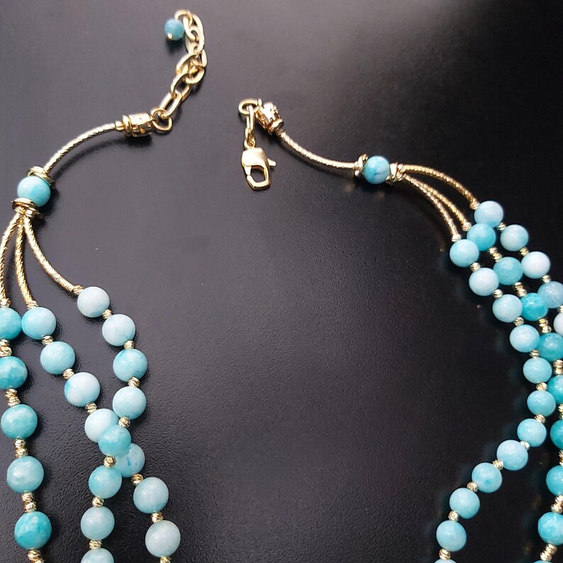 May include: A three-strand necklace with light blue beads and gold accents. The necklace has a lobster claw clasp.