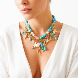 May include: A layered necklace featuring turquoise beads, gold-colored charms, and various pendant shapes. The necklace includes coral, teardrop, and leaf-shaped charms. The necklace is worn against a white background.