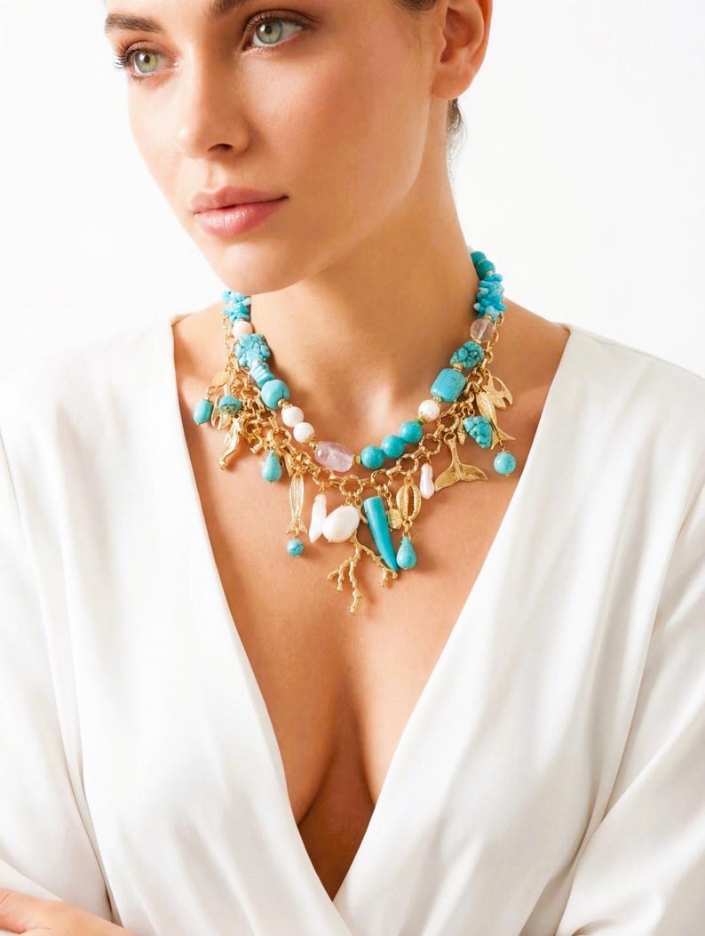 May include: A layered necklace featuring turquoise beads, gold-colored charms, and various pendant shapes. The necklace includes coral, teardrop, and leaf-shaped charms. The necklace is worn against a white background.