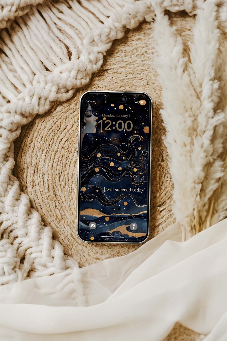 May include: A smartphone shows a celestial wallpaper with a woman's profile, gold details, and the words "I will succeed today." The time is 12:00 on Monday, January 1. The phone is on a textured beige surface.