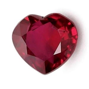 Op de afbeelding: Een hartvormige, gefacetteerde robijn edelsteen. De robijn heeft een diepe, rijke rode kleur met meerdere facetten die licht reflecteren. De edelsteen staat tegen een witte achtergrond.