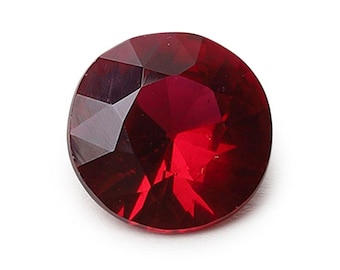 May include: A round, faceted gemstone with a deep, vibrant red color. The stone features a brilliant cut with multiple triangular and kite-shaped facets that reflect light, creating a clear, transparent appearance with sharp, geometric edges.