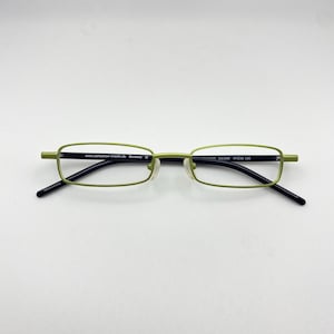 May include: Green rectangular eyeglasses with black temples. The frames have a thin, metallic appearance. The text on the frame reads "www.collection-creativ.de Germany CE" and "AC-411 Col.830 47018 135".