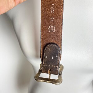 May include: A brown leather belt featuring a weathered texture and a brass-toned metal buckle. The inner side of the belt displays the embossed text 75, 7253, and a stamp reading Echt Leder, indicating genuine leather construction.