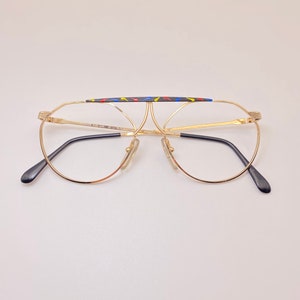 May include: Gold-rimmed round glasses with a black and multi-colored patterned bridge.