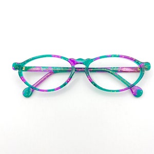 Può includere: Occhiali ovali di colore verde e viola con puntini dorati. Gli occhiali hanno una sottile montatura in metallo.
