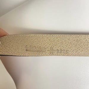 May include: Close-up of a beige leather belt's interior. The belt is marked with the text "CUERO VACA" and "INDUSTRIA ARGENTINA". The size is indicated as 36 and 90, with the number 8806 also visible.
