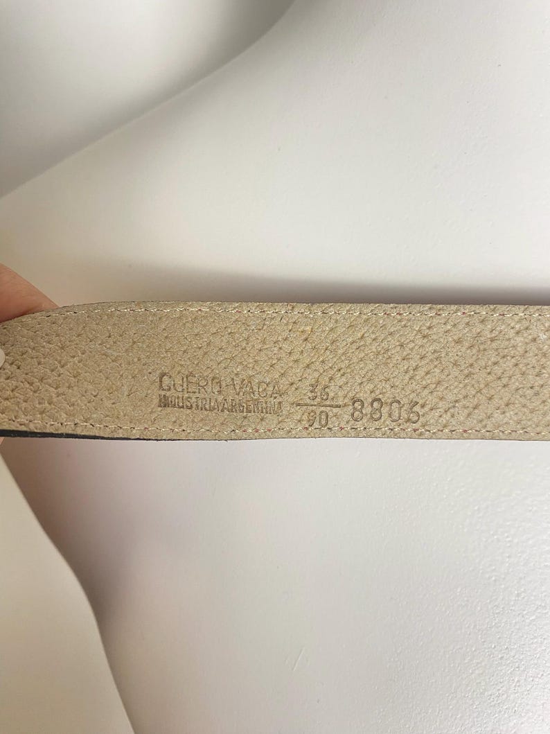 May include: Close-up of a beige leather belt's interior. The belt is marked with the text "CUERO VACA" and "INDUSTRIA ARGENTINA". The size is indicated as 36 and 90, with the number 8806 also visible.
