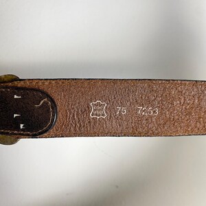 May include: A brown leather belt featuring a stamped emblem with the text ECHT LEDER, the number 75, and the number 7253. The belt has a dark brown edge and a metallic buckle visible on the left side, showing a textured surface and clear markings.