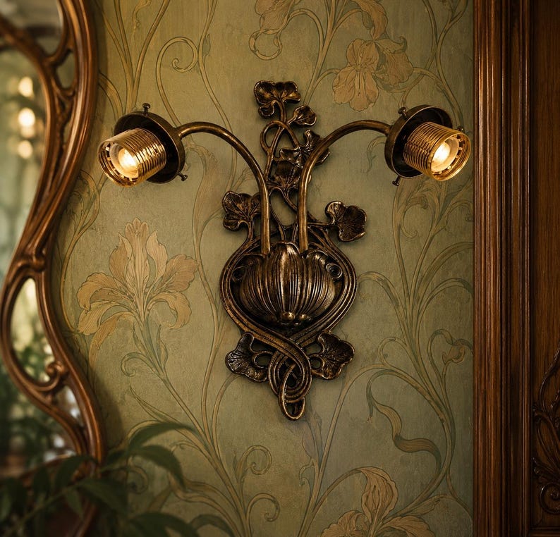May include: A dual-arm wall sconce featuring a dark bronze finish with intricate leaf and vine detailing. The fixture has two cylindrical light sockets with exposed bulbs, extending from a central bulbous base mounted on a wall.