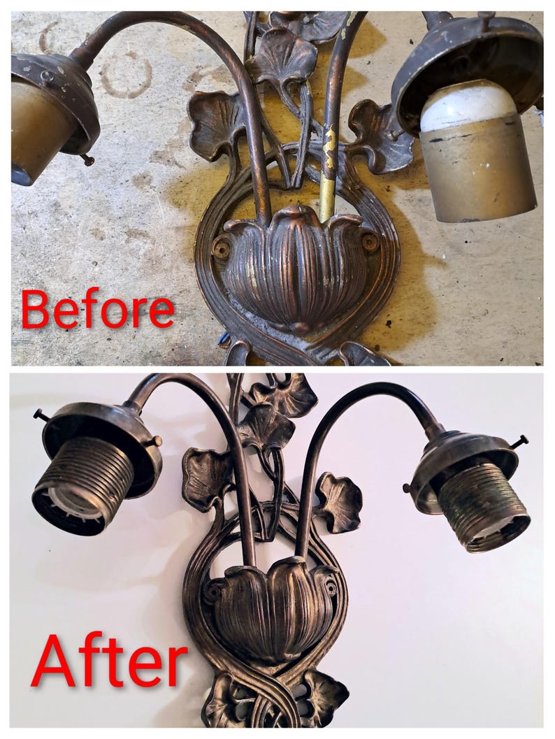 May include: A two-light wall sconce featuring a dark bronze-toned metal finish with floral and leaf motifs. The fixture includes two curved arms extending from a central base shaped like a flower bud, with two threaded light bulb sockets attached.