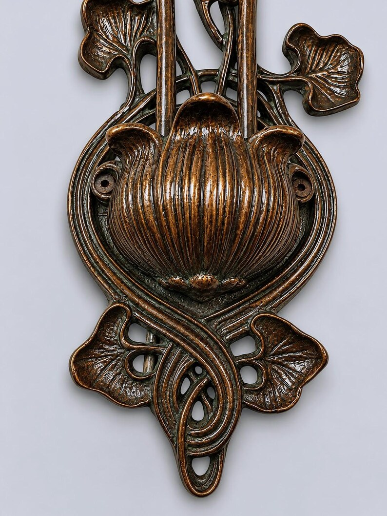 May include: A bronze-toned metal wall plate featuring a central fluted flower bud design surrounded by stylized leaves and curved stems. The decorative piece includes two circular mounting holes on the sides and an elongated, symmetrical vertical structure.