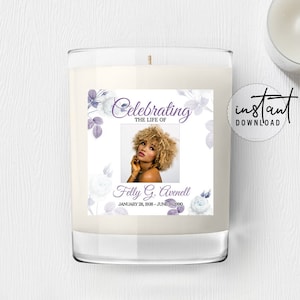 Könnte beinhalten: Eine weiße Kerze mit einem Etikett, auf dem "Celebrating the Life of" steht und ein Foto einer Frau mit lockigem Haar zu sehen ist. Das Etikett enthält auch den Text "Felly G. Avenell" und die Daten "January 28, 1938 - June 18, 1900". Das Etikett ist mit einem floralen Design in Violett- und Weißtönen verziert.