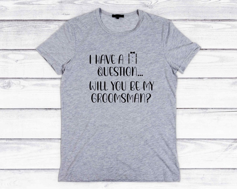 K&ouml;nnte beinhalten: Graues T-Shirt mit schwarzem Text, der lautet: "Ich habe eine Frage... Willst du mein Trauzeuge sein?"