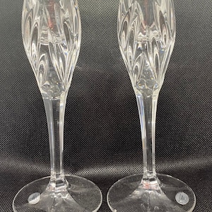 May include: Two clear glass candle holders with a cut glass design. The candle holders have a tall, slender stem and a wide base.