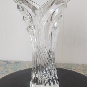 May include: Clear glass vase with a flared, petal-like top and a twisted, ribbed design. The vase has a cylindrical base and a tall, elegant shape, suitable for floral arrangements or decorative display.