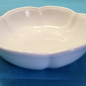 May include: A white ceramic bowl with a scalloped edge. The bowl is empty and has a smooth, glossy finish.