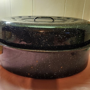 May include: A black enamel roasting pan with a lid. The pan has a speckled white finish and a gold-colored handle.