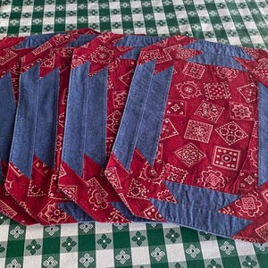 May include: Set of five red and blue placemats with a bandana print. The placemats are made of fabric and have a denim border.